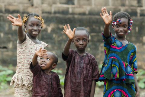 Group of children smiling and waving together, representing community support, child development, education, and nonprofit outreach programs.